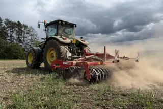Traktor s červeným podmítačem SMS Agro na poli